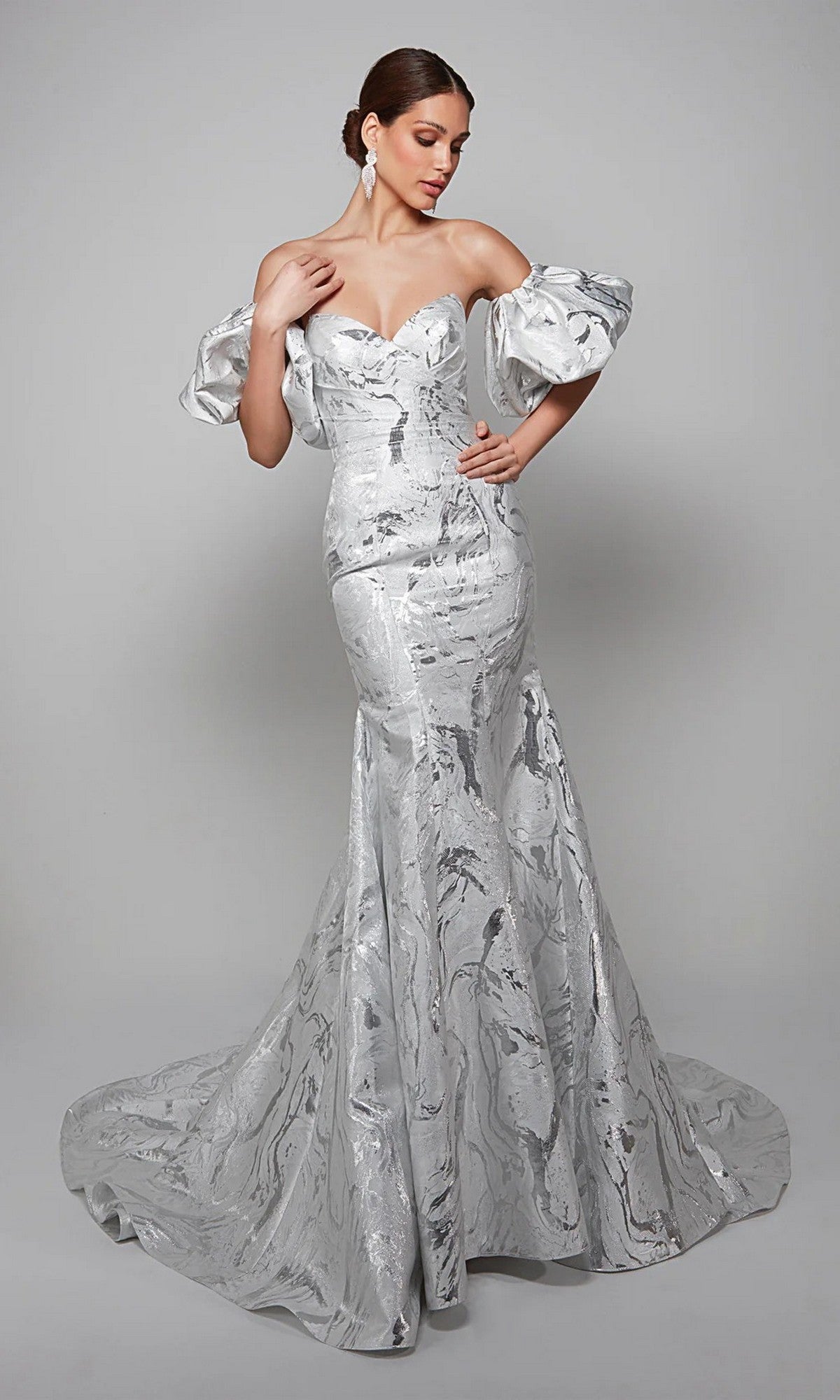 A woman poses elegantly in the Alyce 7055 Long White Dress, featuring puffed sleeves and a subtle marble pattern—a stunning mother-of-the-bride gown against a plain gray background.